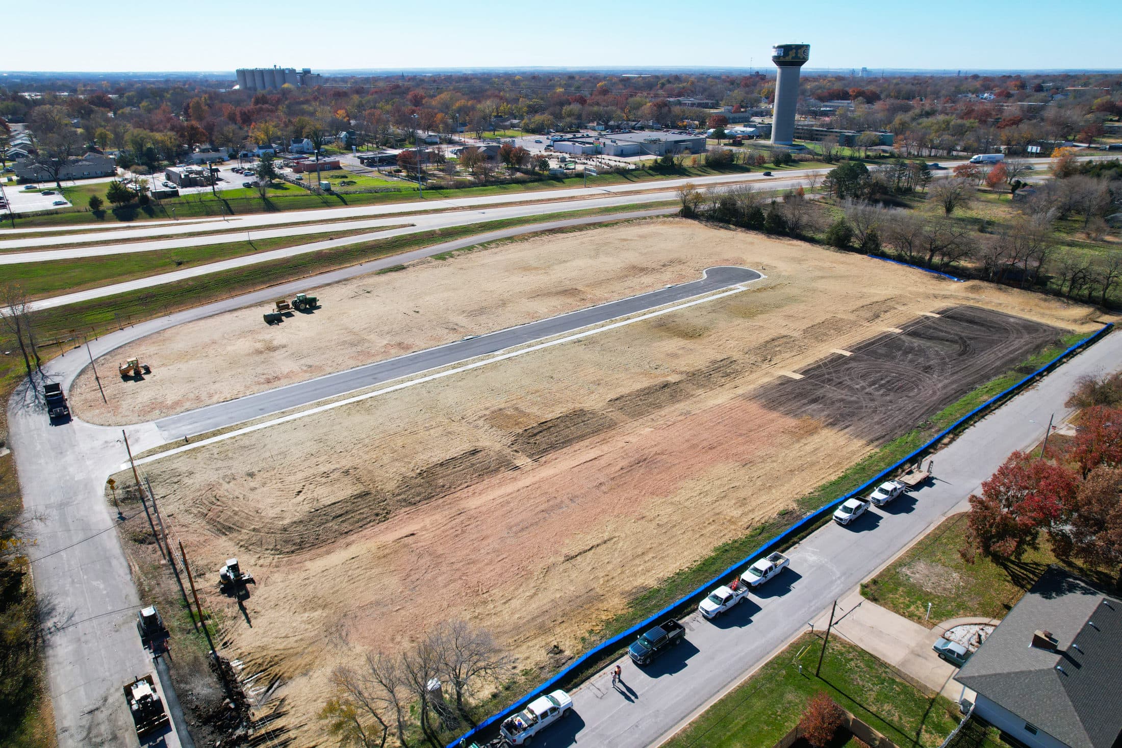 Aerial view of Mahnopoly Avenue mid-construction — the freshly paved street and curbed lots, with a water tower in the distance.